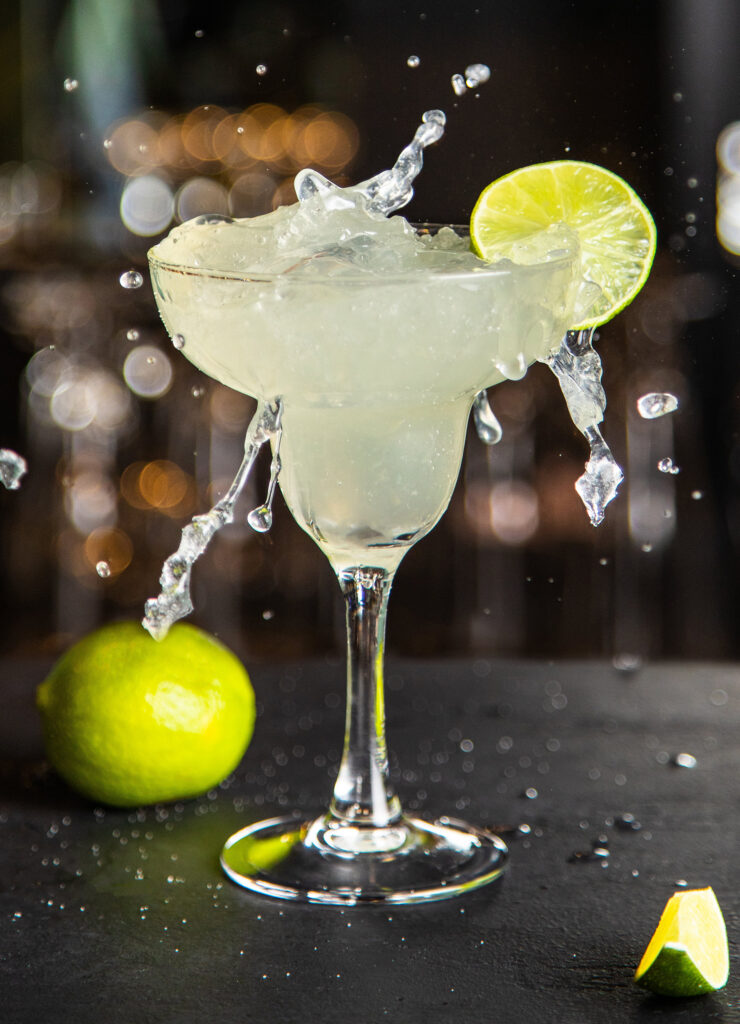 Margarita in a glass with lime in a glass on dark background, nuts and greens